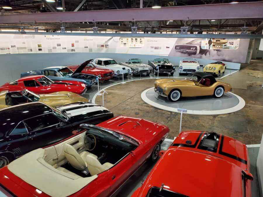 Experience the charm of the Edge District at a classic car exhibit. Discover a showcase of timeless vintage models arranged in a captivating circle, with a gold convertible stealing the spotlight at the center. 