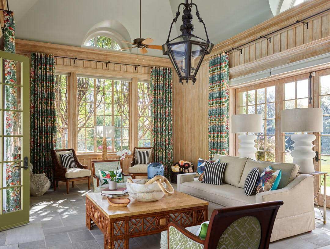 A well-lit living room designed by expert home builders, featuring large windows, patterned curtains, a beige sofa, a wooden coffee table, and various decorative items.