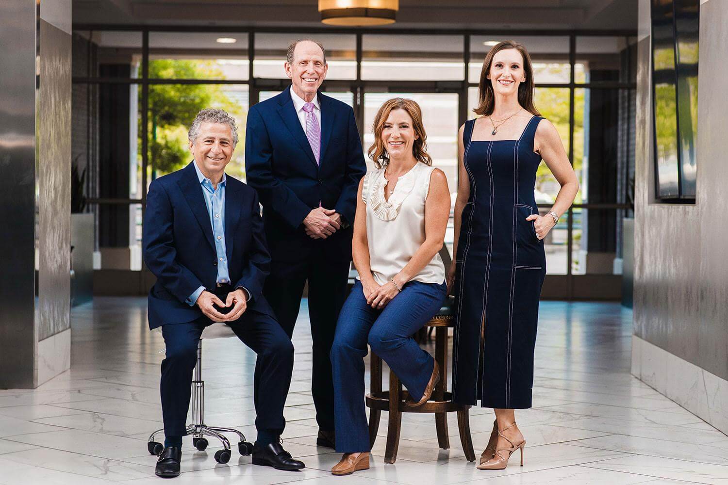Four professionally dressed adults pose together in a modern, well-lit hallway at one of The Top Med Spas in Memphis; two are standing, one is seated on a stool, and one sits on a chair.