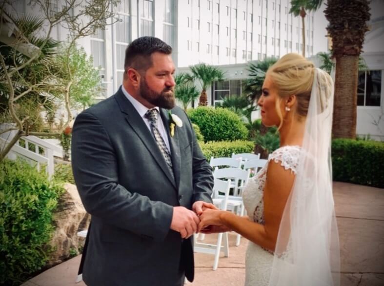 They Had the Last Pre-COVID Wedding in Vegas! - 7 A couple stands together outdoors at a Las Vegas wedding, with the man in a suit and the woman in a wedding dress, facing each other and holding hands.