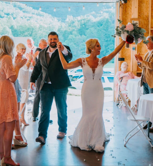 They Had the Last Pre-COVID Wedding in Vegas! - 12 Bride and groom, glowing with joy, hold hands and celebrate as they make their grand entrance into the wedding reception area, surrounded by applauding guests. The bride clutches her bouquet with delight.
