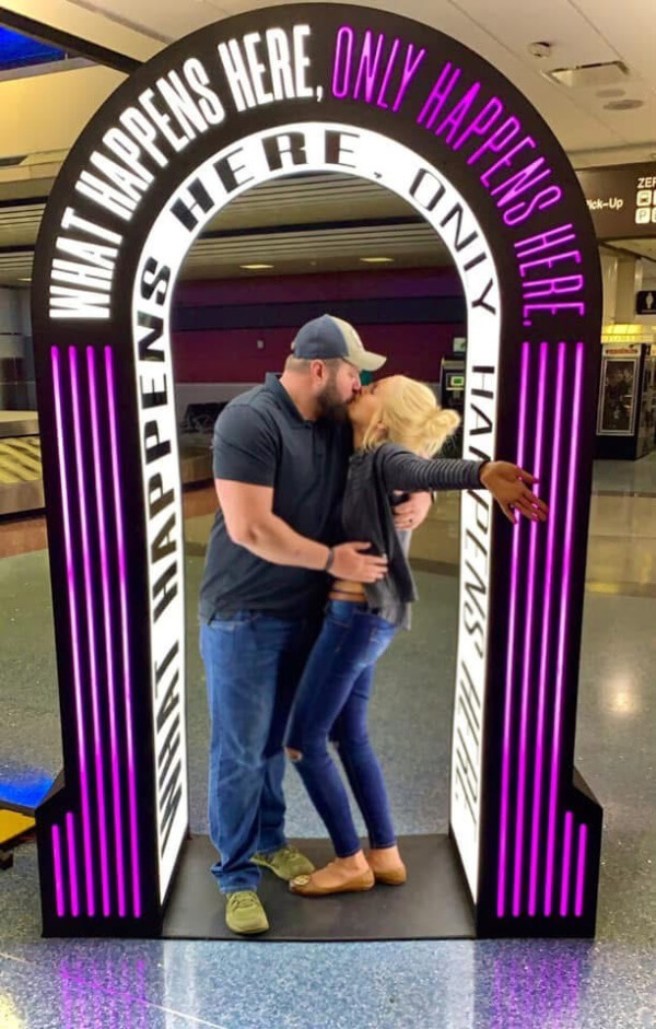 They Had the Last Pre-COVID Wedding in Vegas! - 1 A couple is sharing a kiss inside an archway, with the neon-lit words "What Happens Here, Only Happens Here" glowing above—a perfect backdrop for a Las Vegas wedding moment.