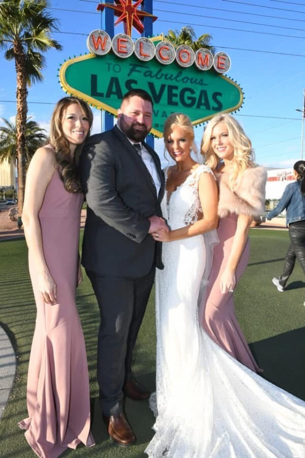 They Had the Last Pre-COVID Wedding in Vegas! - 10 A bride and groom stand beneath the Las Vegas wedding side with female friends on either side.