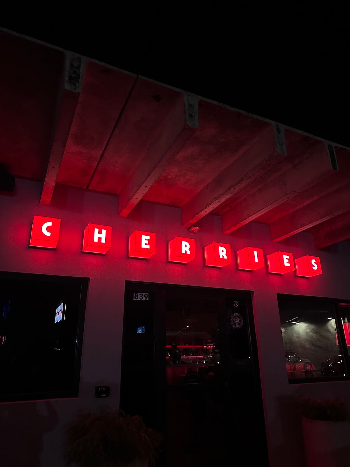 Red neon sign displays the word "CHERRIES" on a building at night.