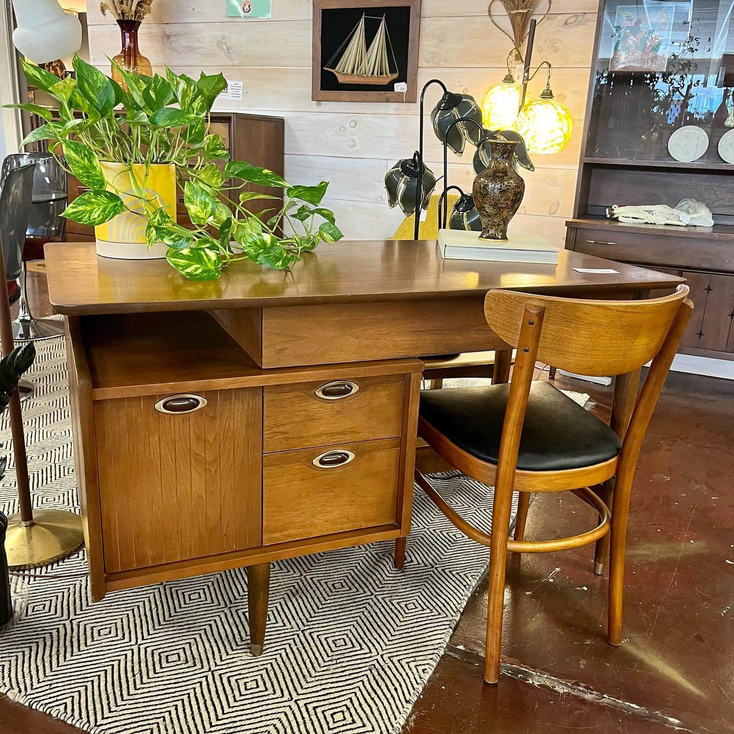 Nashville's Vintage Retail Trail: 8 Must-Visit Home Decor Spots - 6 Mid-century modern wooden desk with drawers and a matching chair, topped with a green potted plant, lamps, and decorative items from Nashville vintage stores, set on a patterned rug in a well-lit room.