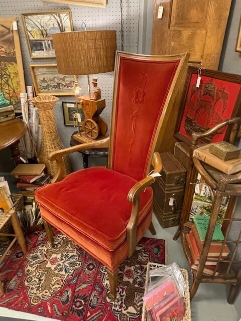 Nashville's Vintage Retail Trail: 8 Must-Visit Home Decor Spots - 5 Vintage red velvet armchair with a high back, nestled among antiques and paintings on a patterned rug in one of Nashville's vintage stores, offers a touch of timeless elegance.