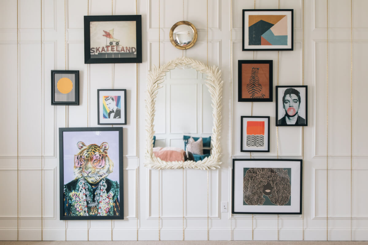 A wall adorned with a captivating array of framed artwork, including abstract designs, portraits, and a mirror with a decorative frame centered among them.