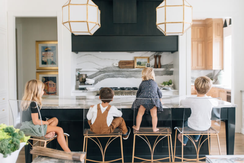 Four children sit on bar stools at a kitchen counter with a black and white backsplash.
