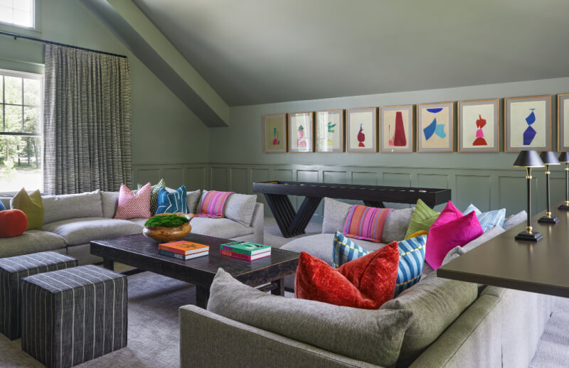 A modern City Hill living room features gray sectional sofas, colorful cushions, a dark wood coffee table, abstract art on the walls, and a large window with striped curtains.