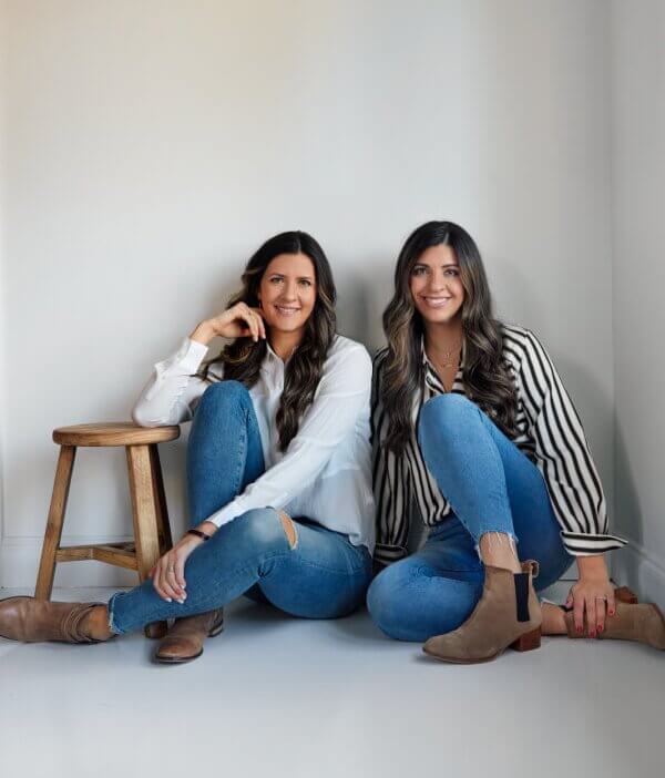Two women sit on the floor, another perches on a stool, all in jeans and ankle boots against a plain white backdrop, exuding casual urban vibes reminiscent of City Hill.