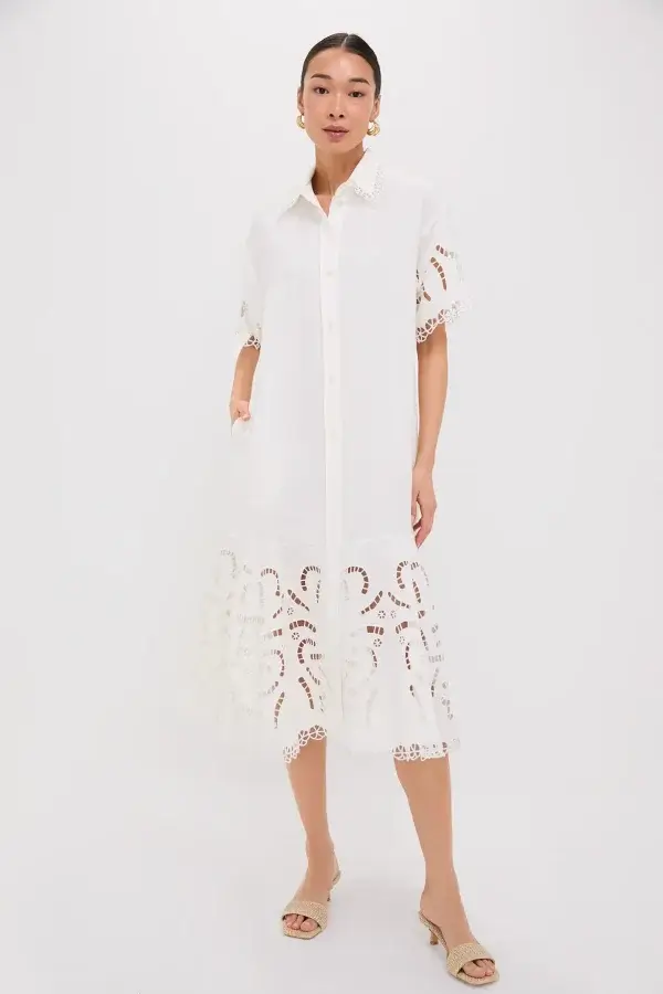 Woman in a white button-up midi dress with crochet details at the hem, standing with hands in pockets, wearing nude slide sandals. A modern spin on classic pieces, perfect for your spring wardrobe essentials.