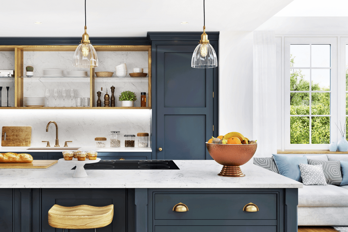 Modern kitchen with navy cabinets, marble countertops, open shelves, hanging pendant lights, and a bowl of fruit on the island; a window seat is visible in the background—crafted by top home builders in Birmingham.