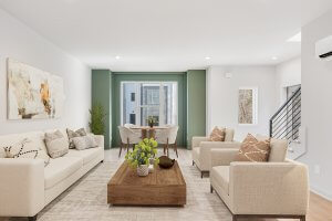 Nestled on E Village Ln, this modern Nashville living room features beige sofas, a wooden coffee table, and abstract wall art. A small dining area by large windows complements the green accent wall and minimalist decor.