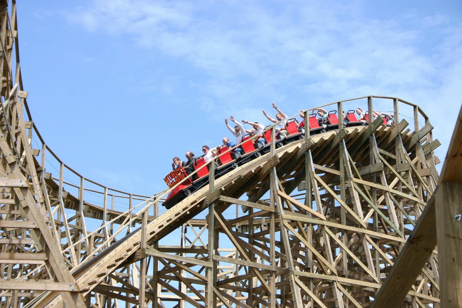7 Best Family Vacations for Outdoor Fun - 9 A red roller coaster car glides along a wooden track, with people raising their arms in excitement under a clear blue sky.