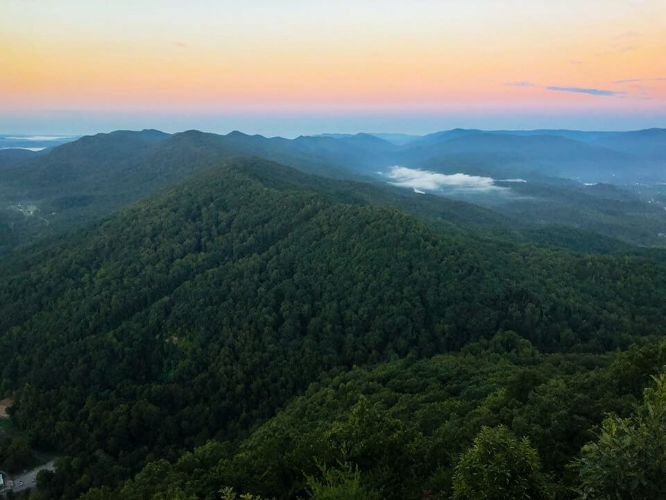 7 Best Family Vacations for Outdoor Fun - 4 Aerial view of lush green mountains at sunrise, perfect for outdoor fun with the family. Light mist graces the valleys as a clear sky shifts from pale yellow to blue, offering one of the best family vacation spots.