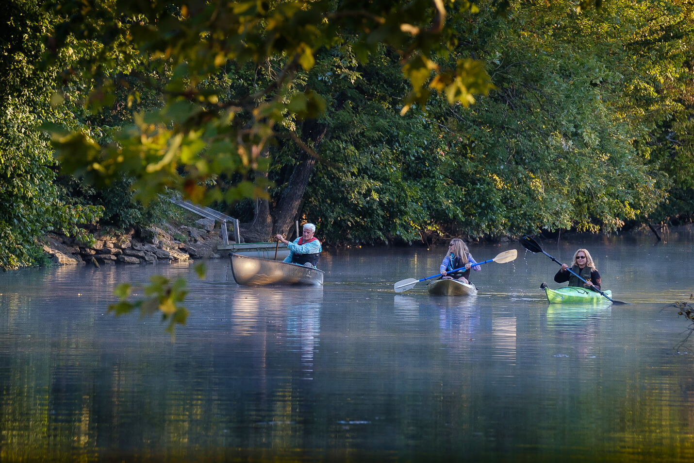 7 Best Family Vacations for Outdoor Fun - 15 Three people are enjoying outdoor fun, paddling on a calm river; two in canoes and one in a kayak, surrounded by lush green trees. It's the perfect scene for family vacations, where nature provides both serenity and adventure.