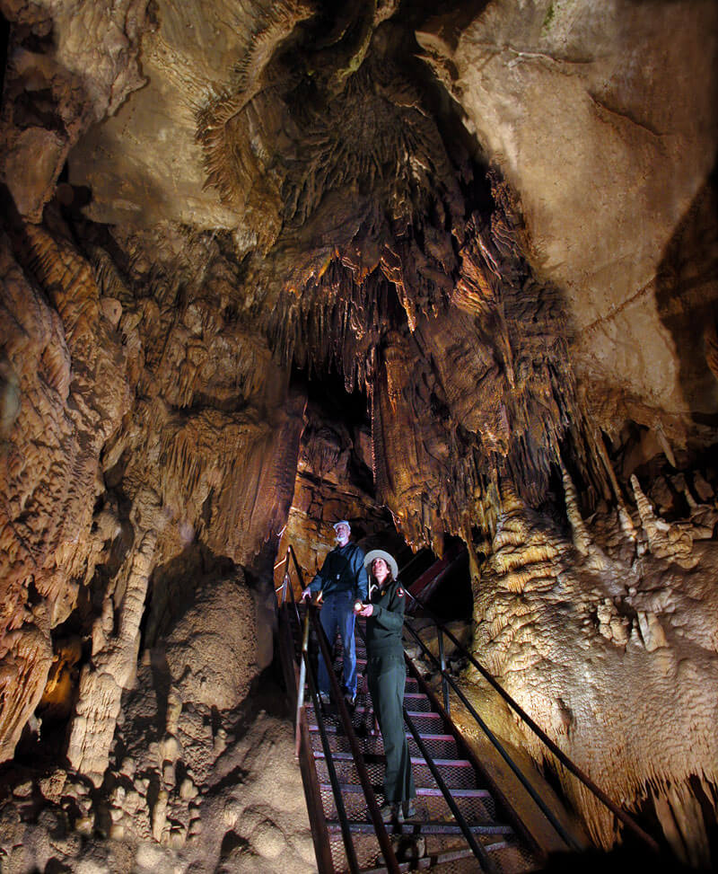 7 Best Family Vacations for Outdoor Fun - 7 Two people stand on a metal staircase inside the cave, surrounded by stalactites and stalagmites.