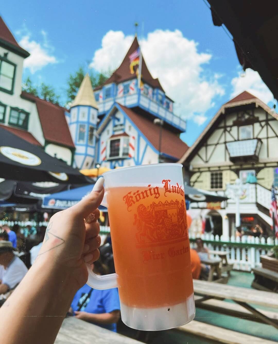 6 Southern Outdoor Getaways for the Adventure Traveler - 4 An adventure traveler raises a large mug of beer in an outdoor setting, with colorful Bavarian-style buildings painting the backdrop under a clear blue sky.