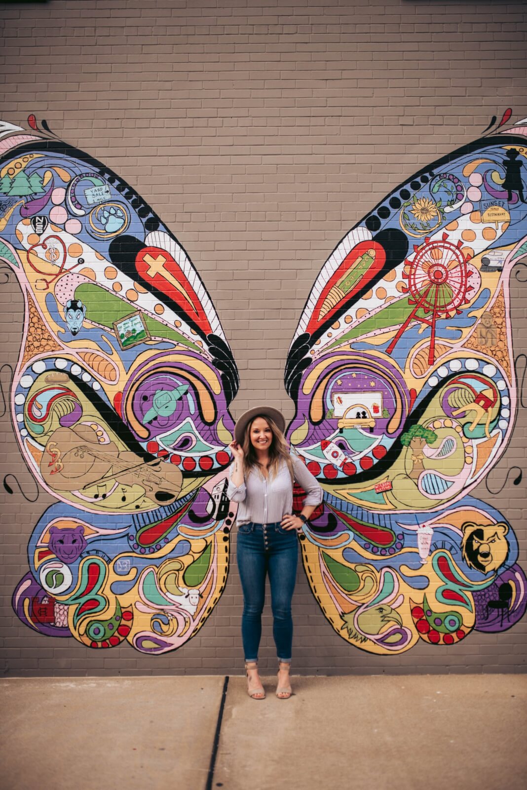 A person stands in front of a mural with colorful butterfly wings painted on a brick wall in the heart of Tennessee's historic downtowns.