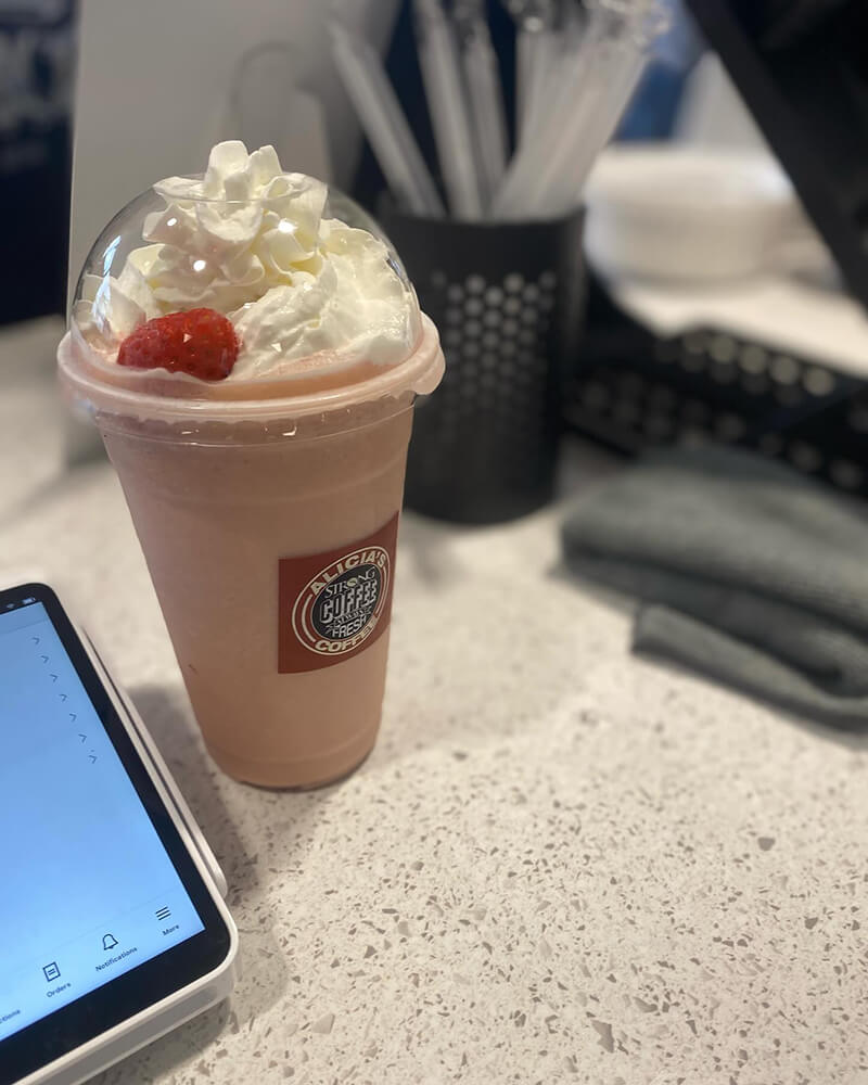A strawberry milkshake, complete with a swirl of whipped cream and a cherry, sits invitingly beside a tablet on the white counter.