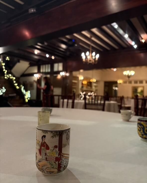 A dimly lit restaurant in Birmingham features decorative wooden beams. A porcelain cup with colorful designs sits on a round table, while fairy lights illuminate a staircase in the background.