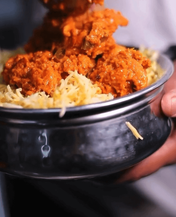 In a stainless steel bowl, a person serves a flavorful curry dish over a bed of rice—perfect to try this month for those exploring new restaurants in Birmingham.