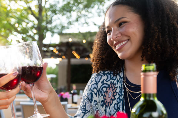 At the Santé South Wine Festival, two people clink wine glasses outdoors, with a smiling woman in focus. A bottle of wine graces the table, capturing the spirit of joyful celebration.