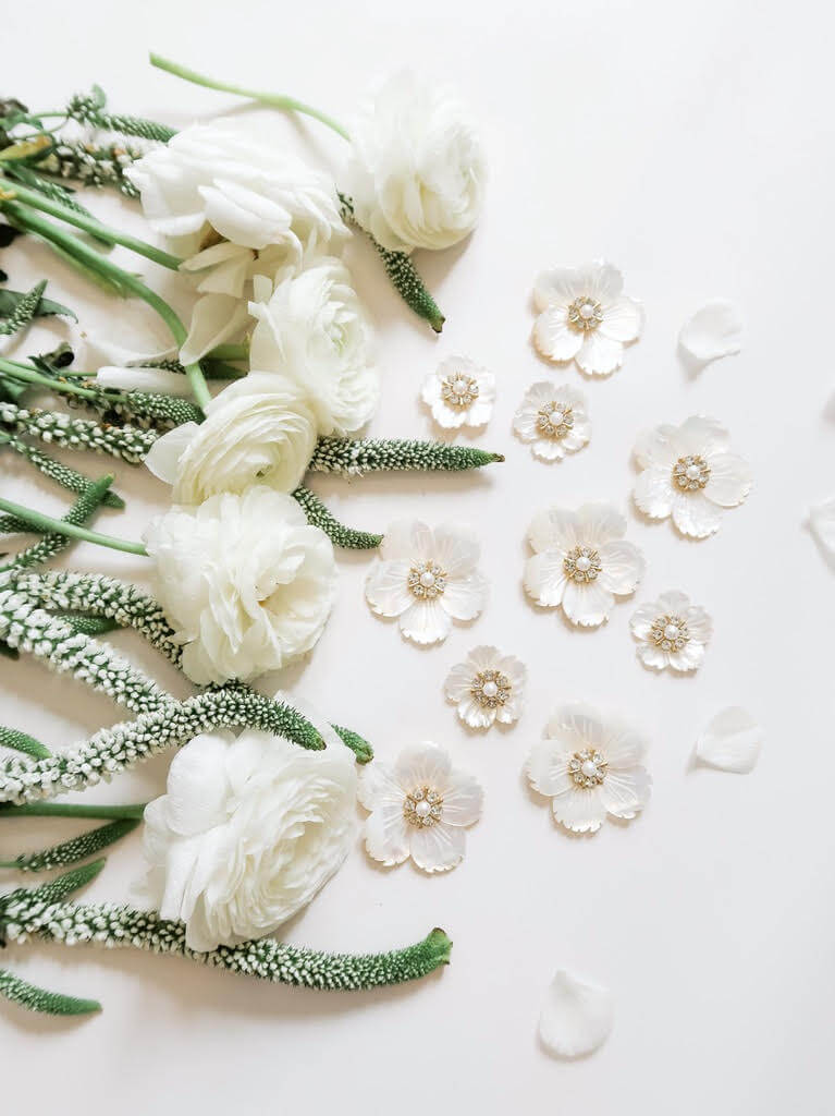 White flowers and small blossoms with decorative centers are arranged on a pale surface, reminiscent of an SJ Bailey design, with a few scattered petals nearby.