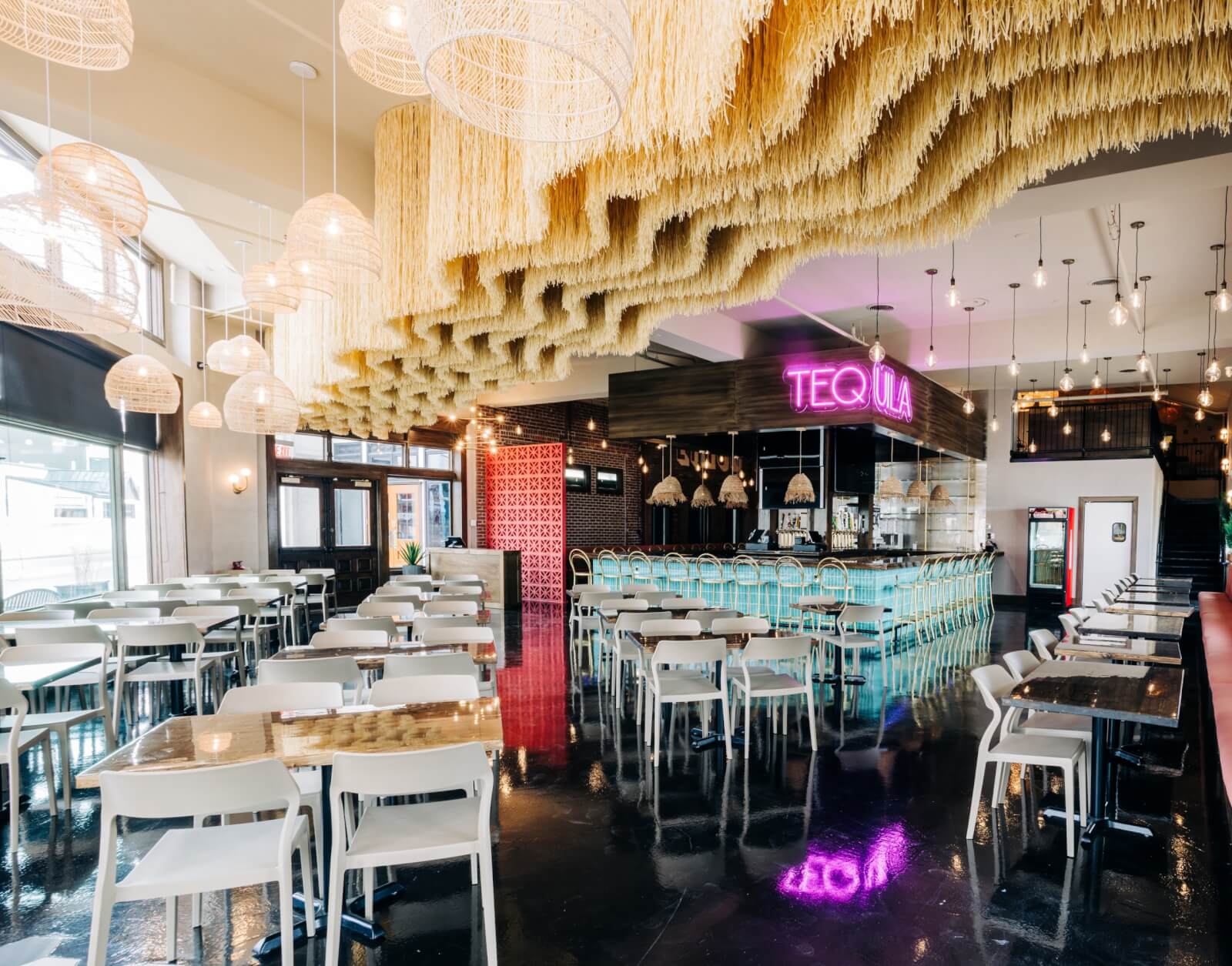 Modern Louisville restaurant interior with white tables and chairs, a neon "Tequila" sign above the bar, wavy ceiling decor, and woven light fixtures. Discover our new menus that perfectly complement the vibrant atmosphere.