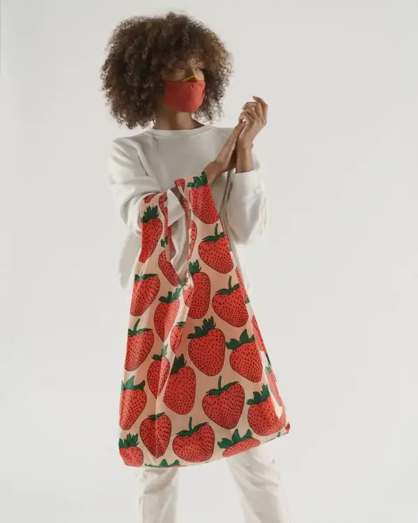 In a vibrant April afternoon in Memphis, a person dons a red mask and white outfit, effortlessly carrying a large tote bag adorned with a cheerful strawberry pattern—an eye-catching find for sure.