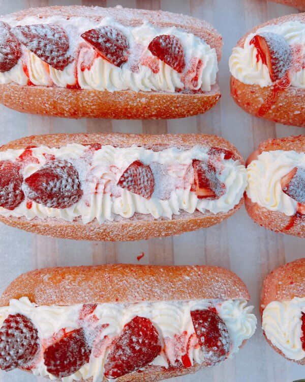 Delectable cream-filled pastries topped with sliced strawberries and dusted with powdered sugar are elegantly arranged in rows.