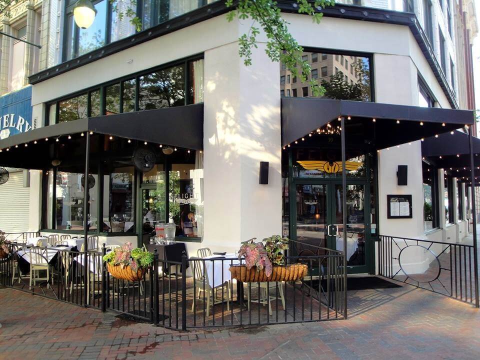 Charming street corner cafe in downtown Memphis, featuring outdoor seating with black awnings, string lights, and potted plants. A true gem in the Memphis dining scene, perfect for those seeking a cozy spot to relax and enjoy.