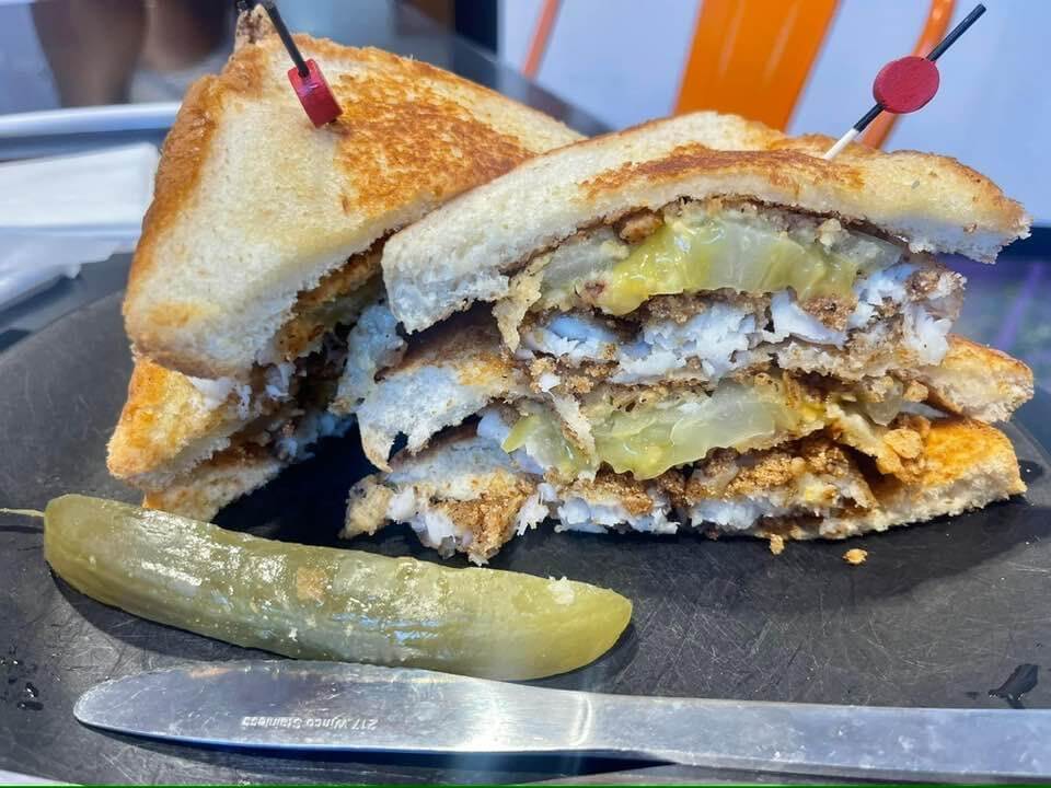 A sandwich on a plate with layers of meat, cheese, and pickles, secured by toothpicks—it's your dining guide to flavors. A pickle spear and a knife are placed beside it, ready to be devoured in the heart of Downtown Memphis.