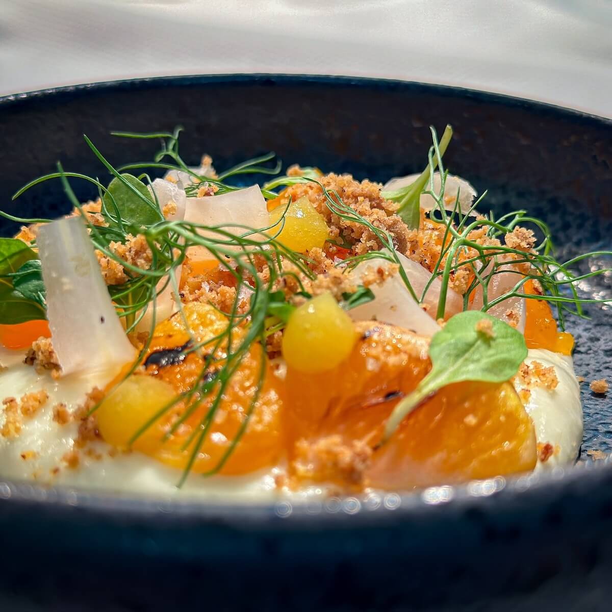 A ceramic plate with creamy yogurt is exquisitely adorned with orange slices, yellow fruit pieces, and leafy greens—a delightful dining guide to the vibrant flavors of Memphis.