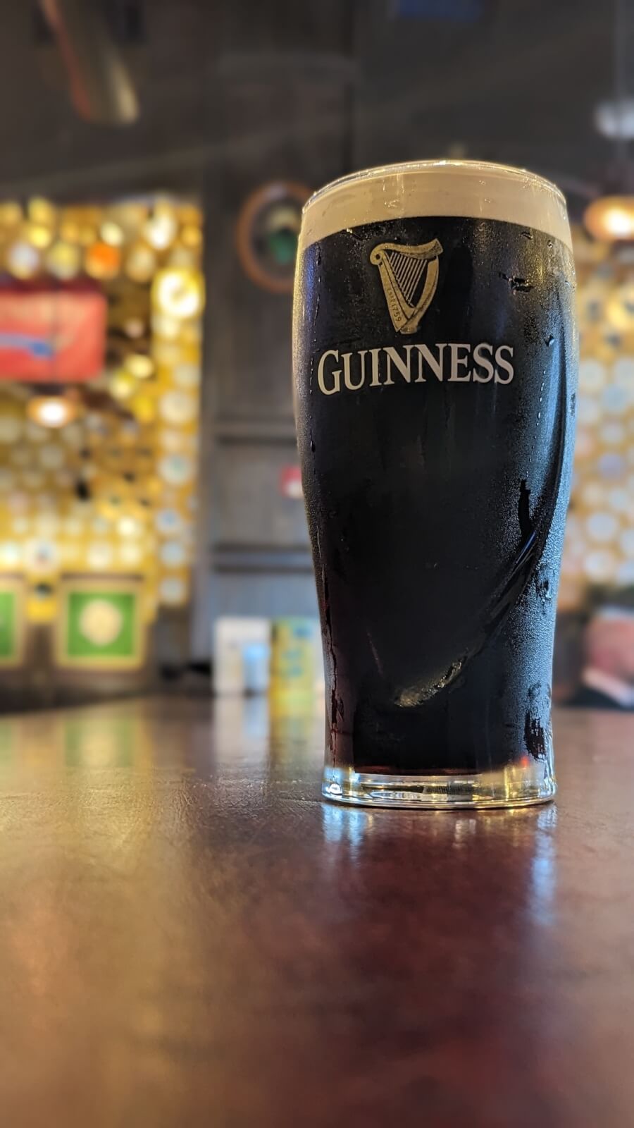 A pint of Guinness beer sits on a wooden bar counter in a cozy pub, as the blurred background hints at Memphis dining charm with its unique wall decor and inviting seating area.