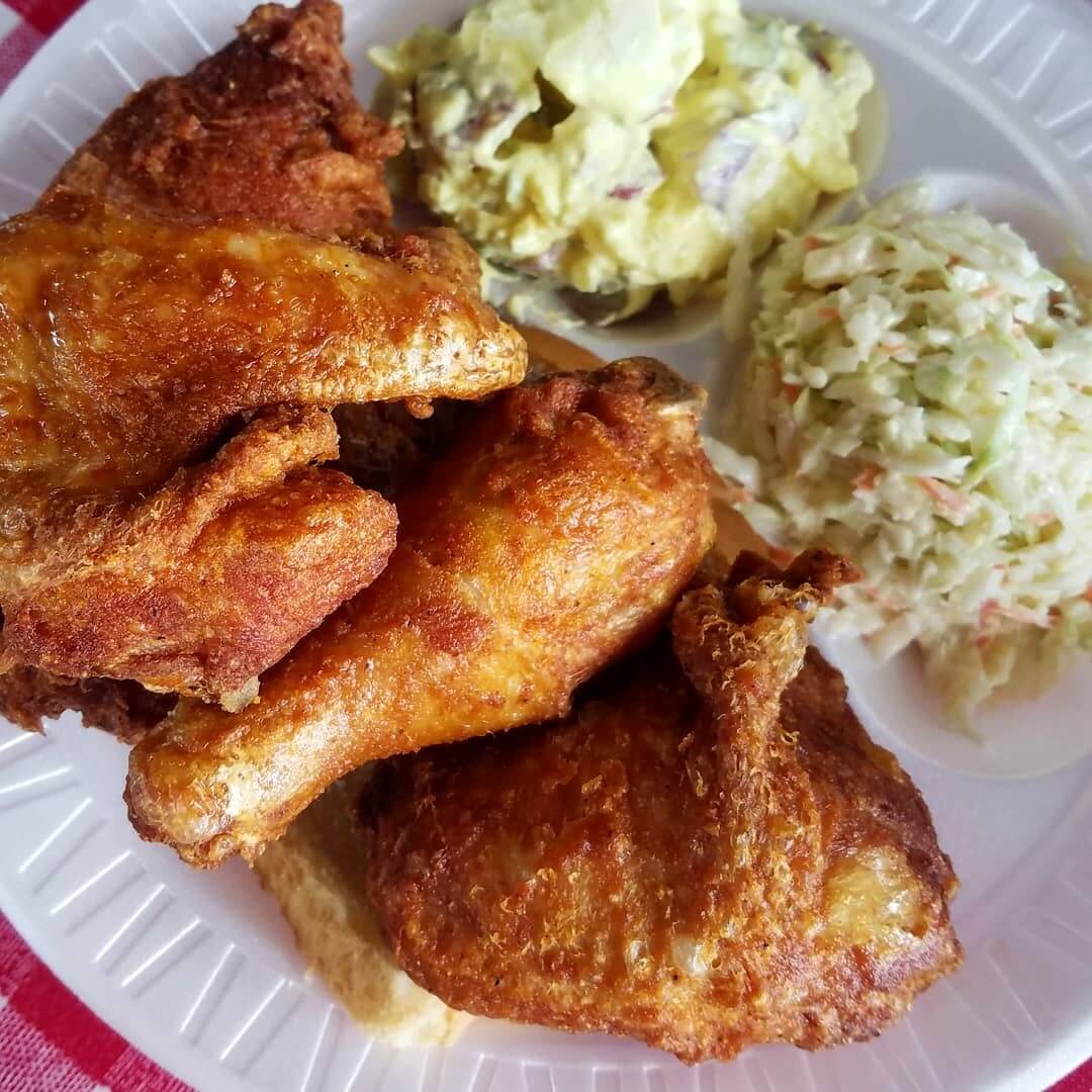 On a red plaid cloth lies a plate featuring crispy fried chicken, creamy potato salad, and tangy coleslaw—a delightful meal to enjoy while exploring Downtown Memphis.