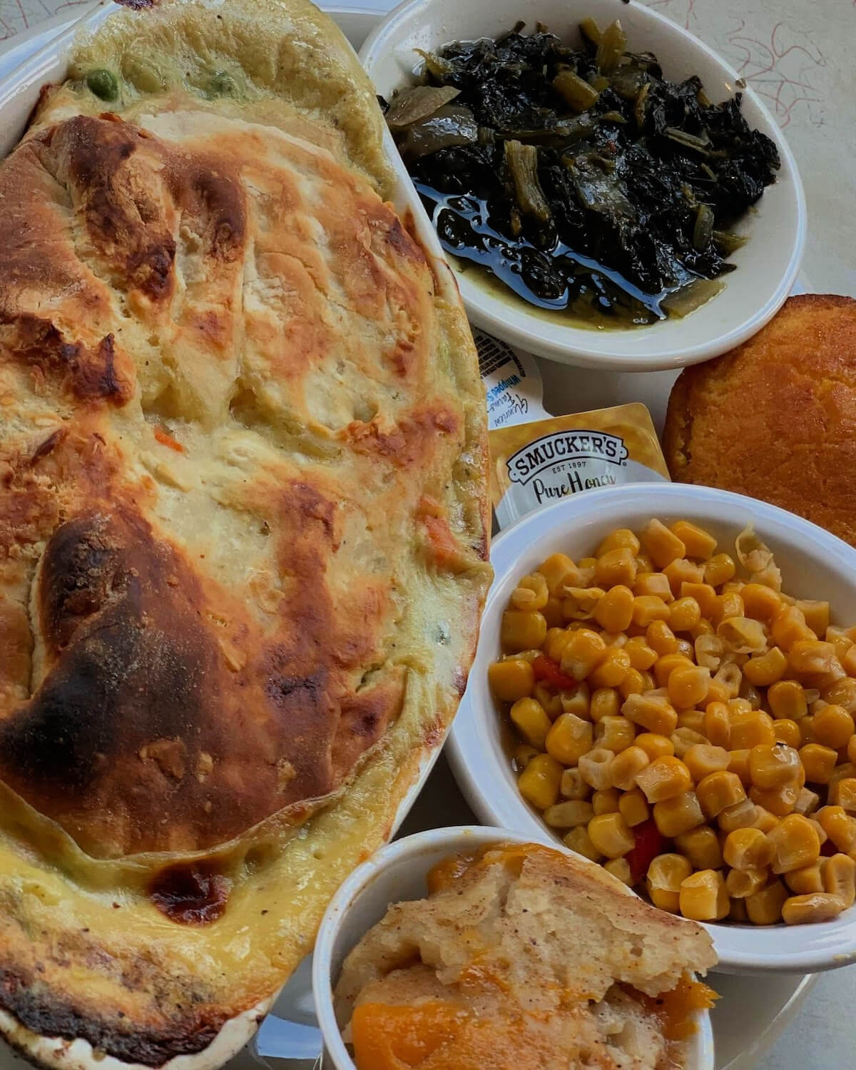 Discover a culinary delight in Downtown Memphis with a baked dish, stewed greens, sweet potato, corn, and peach cobbler presented in separate bowls. 