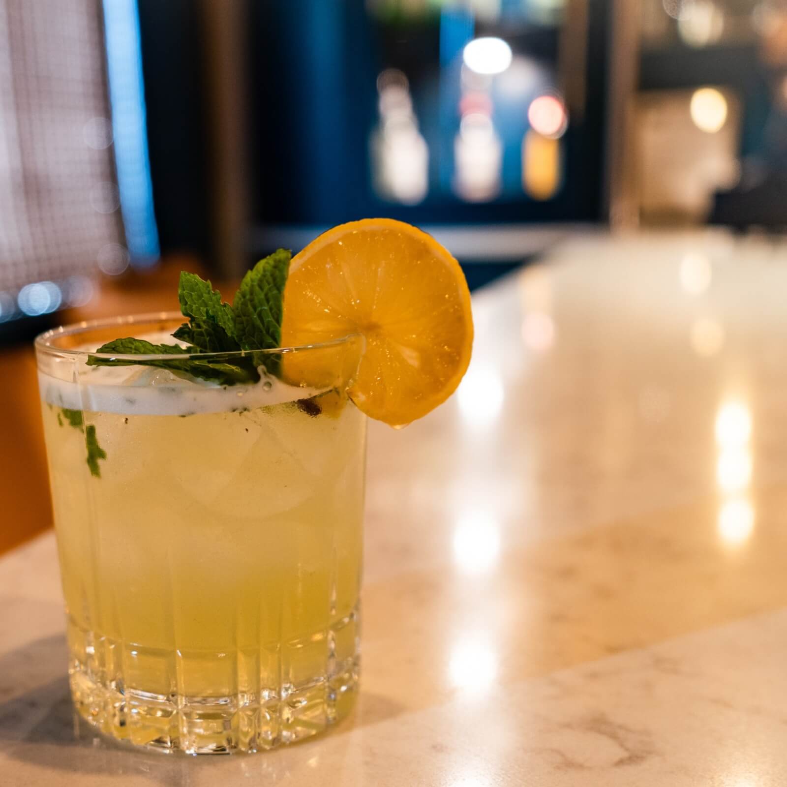 A cocktail with ice, garnished with a lemon slice and mint leaves, sits invitingly on a marble countertop, reminiscent of refreshing trails along the Mississippi.