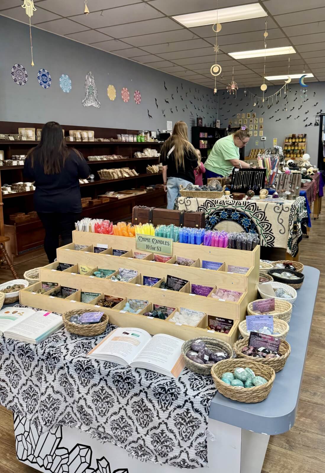Customers in a charming Cynthiana, Kentucky shop browse crystals, candles, and spiritual decor. Shelves and tables display colorful products while walls showcase decorative symbols and artwork, creating a warm and inviting atmosphere unique to Cynthiana KY.
