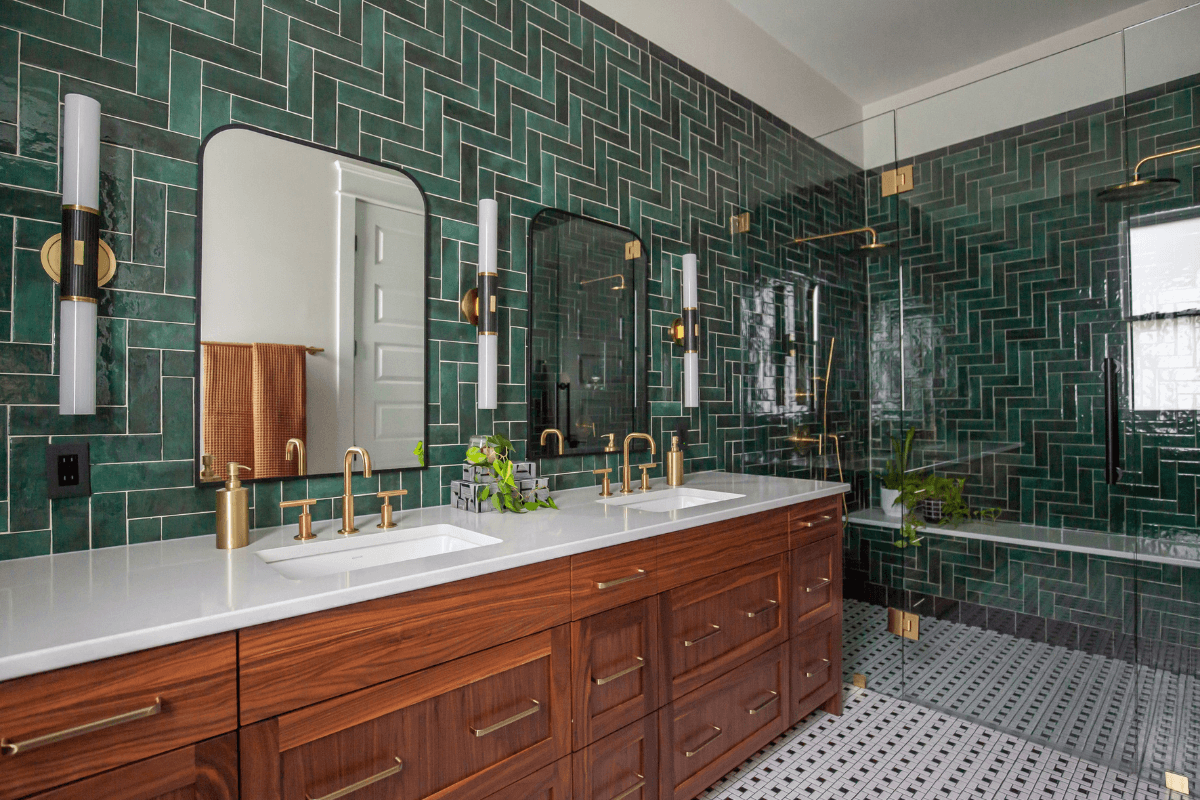 Modern bathroom with green tile walls, double sinks on a wooden vanity, gold fixtures, and a glass-enclosed shower—a stunning retreat crafted by the Best Interior Designers in Nashville.