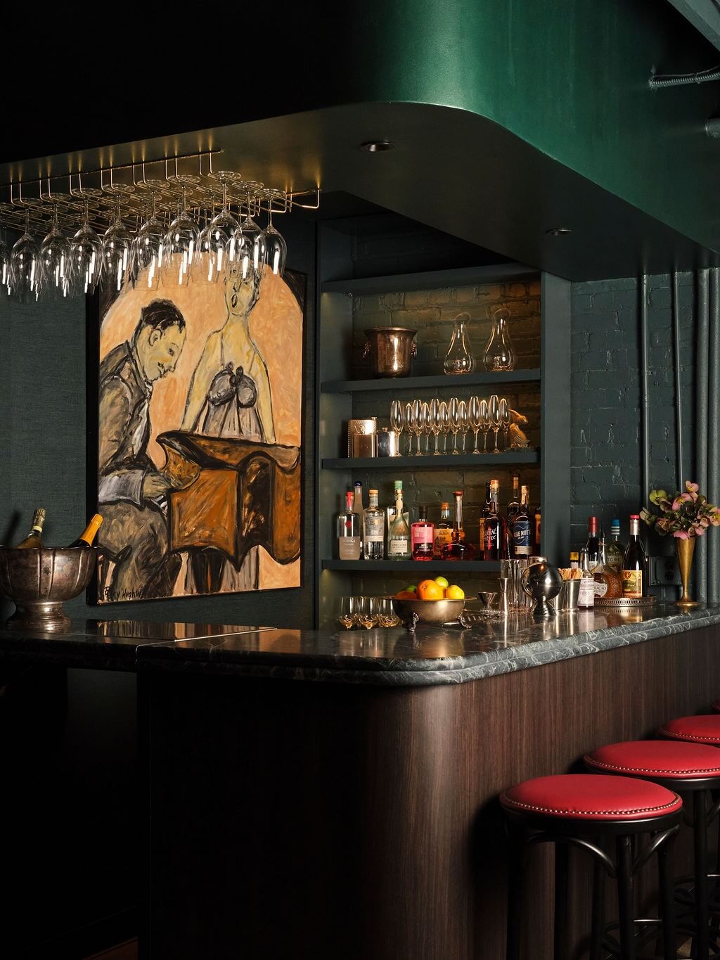 A dimly lit bar in one of the top new Memphis restaurants, featuring a marble countertop, red barstools, shelves of glassware and liquor bottles, and a painting of a pianist on the wall.