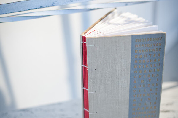 Open book with Coptic binding and red threading on a light surface. Gold text is printed vertically on the gray cover, reminiscent of vintage book covers.
