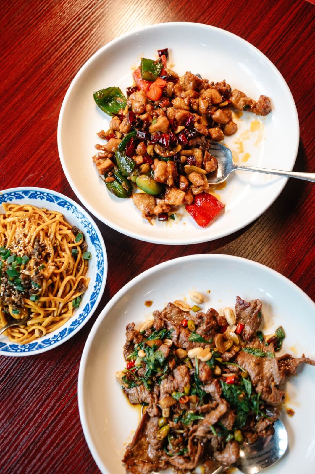 Three dishes on a table at this Memphis restaurant: stir-fried chicken with vegetables, spicy beef with herbs, and a bowl of noodles with sesame seeds and greens.