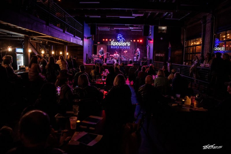 A band performs on stage at Rooster's Blues House, surrounded by a seated and standing audience in the dimly lit venue, reminiscent of the vibrant atmosphere found in Memphis eateries.