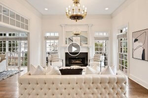 Elegant Collierville living room with a tufted sofa, black fireplace, and two patterned chairs. Large windows and a glass-paned door allow natural light. A gold chandelier hangs from the ceiling, reflecting Tennessee charm in every corner.