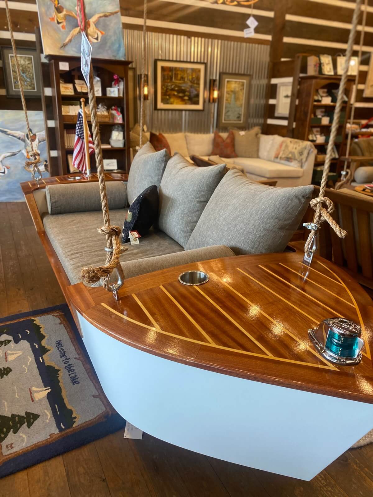 A wooden boat-shaped swing with cushions and ropes hangs indoors, surrounded by shelves, artwork, and decor—capturing the cozy charm found in the best home and gift stores in Birmingham.