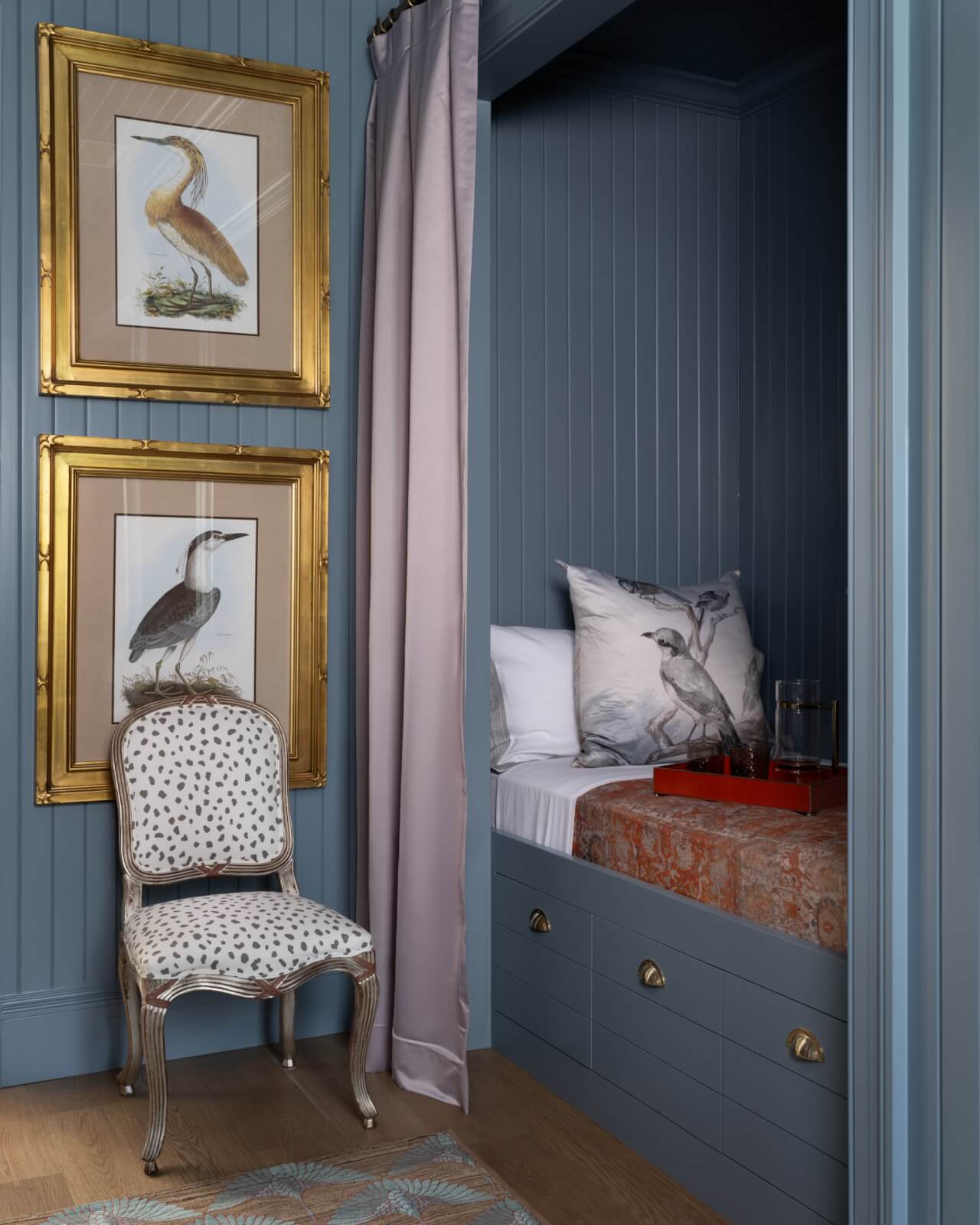 A blue color-drenched bedroom features a built-in single bed anf bird wall art.