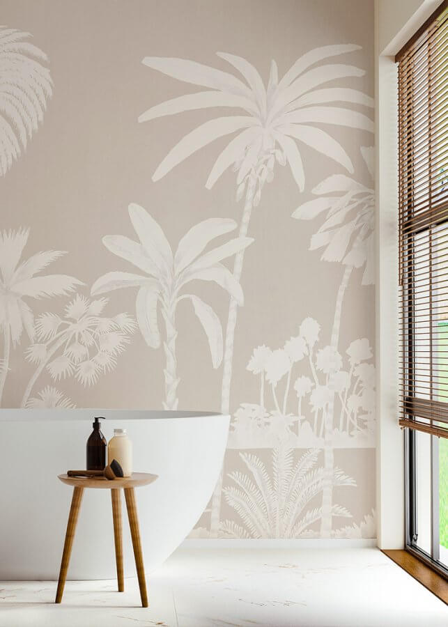 Modern bathroom with a freestanding white bathtub, a small wooden stool holding bottles, and a large wall mural featuring white palm tree silhouettes. Light filters through brown blinds.