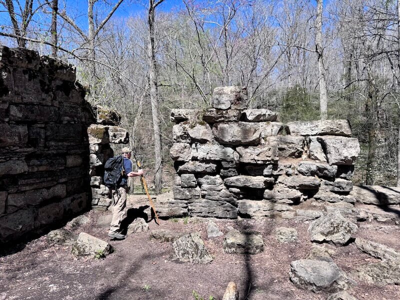 A person with a backpack explores ancient stone ruins surrounded by leafless trees under a clear Nashville sky, completing their 3-Mile Hike.