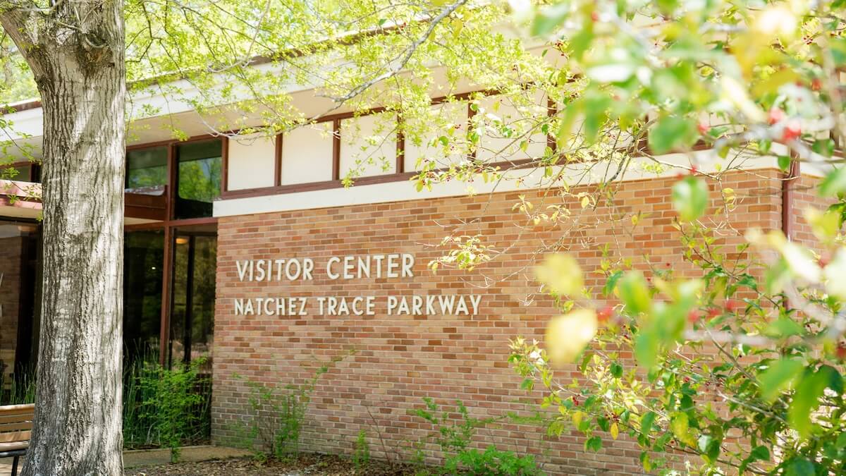 A brick building with a sign reading "Visitor Center Natchez Trace Parkway" sits amid green trees and foliage—a perfect stop for trip planning on a girls trip near Tupelo, MS.